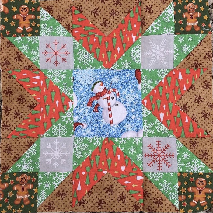 a star cross quilt block in red gold and green there is a snowman in the middle 