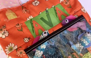 Close up of the handmade tote bag - it says AVA and has a fish tank on the front with Tiddly Fish poking out the pocket